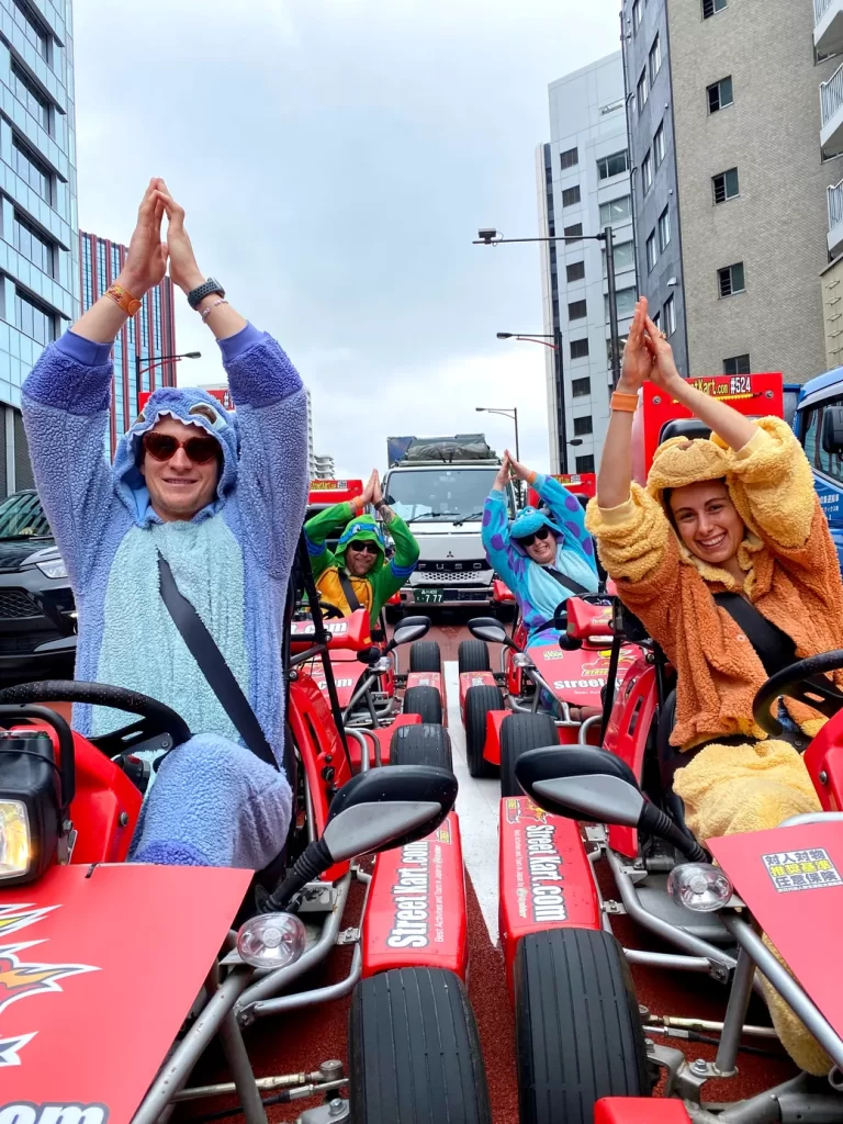 IMG_6155 - StreetKart Group of people in fuzzy animal onesies on red go-karts in an urban street, hands raised together above their heads.